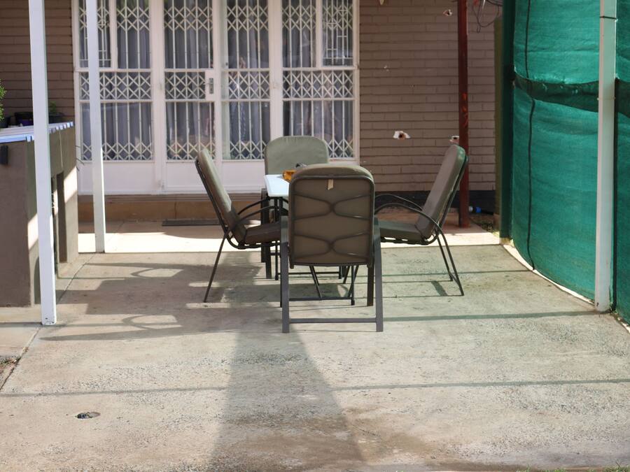 Un patio al aire libre con mesa y sillas, un espacio cubierto y una ventana con rejas.