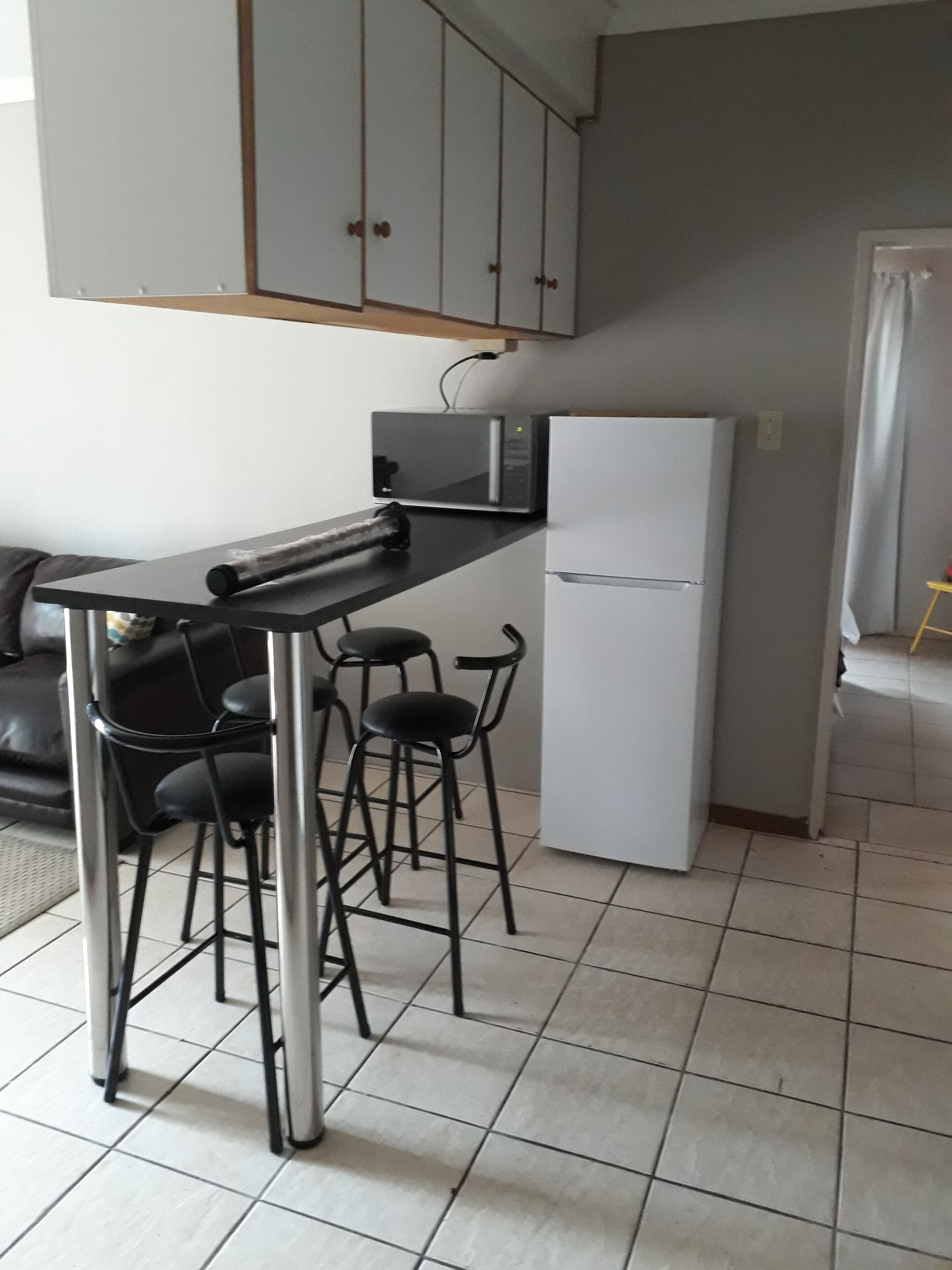 A compact kitchen with a black countertop, a white refrigerator, and a set of black bar stools.