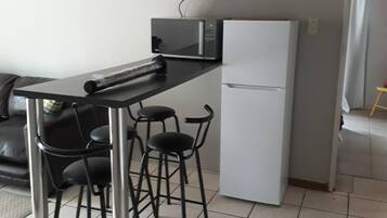 A compact kitchen with a black countertop, a white refrigerator, and a set of black bar stools.
