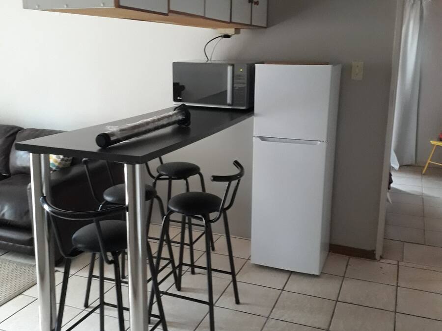A compact kitchen with a black countertop, a white refrigerator, and a set of black bar stools.