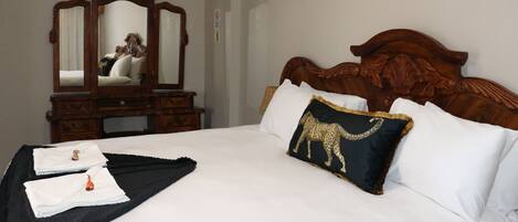 Una cama bien hecha con sábanas blancas, un plaid negro y una almohada con estampado de leopardo.