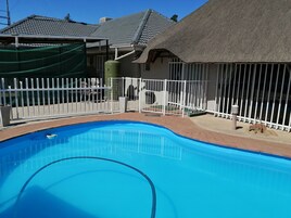Piscina com cerca branca, estrutura de telhado de palha e um alpendre de tijolos.