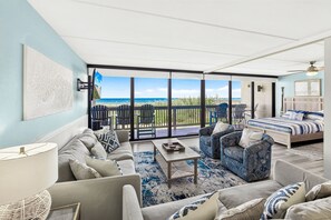 Un salon spacieux doté d’une grande porte-fenêtre coulissante donnant sur un balcon avec vue sur l’océan.