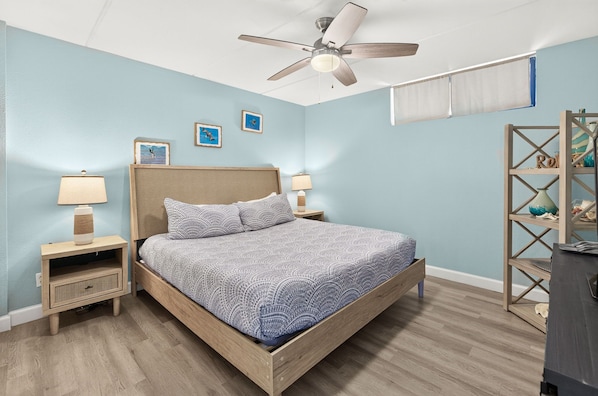 Une chambre à coucher comprenant un lit, des tables de chevet, un ventilateur de plafond et une étagère fixée au mur.