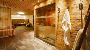 A sauna room with a glass door, wooden walls, and a towel hanging on a hook.