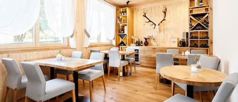 Un interior de madera con mesas y sillas, un botellero y un adorno de cornamenta de ciervo.