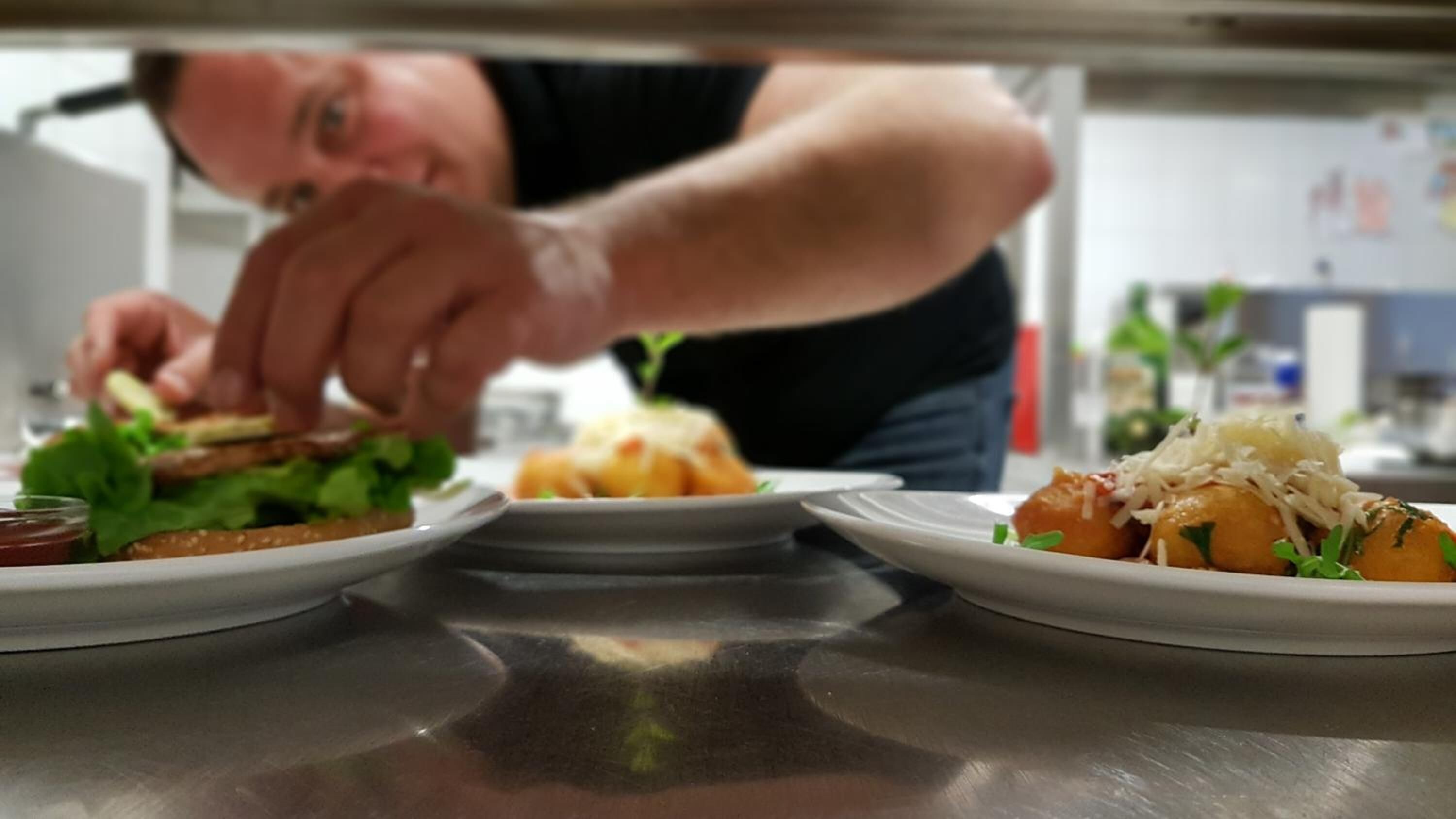 A chef preparing food in a kitchen with stainless steel countertops and a whiteboard in the background.