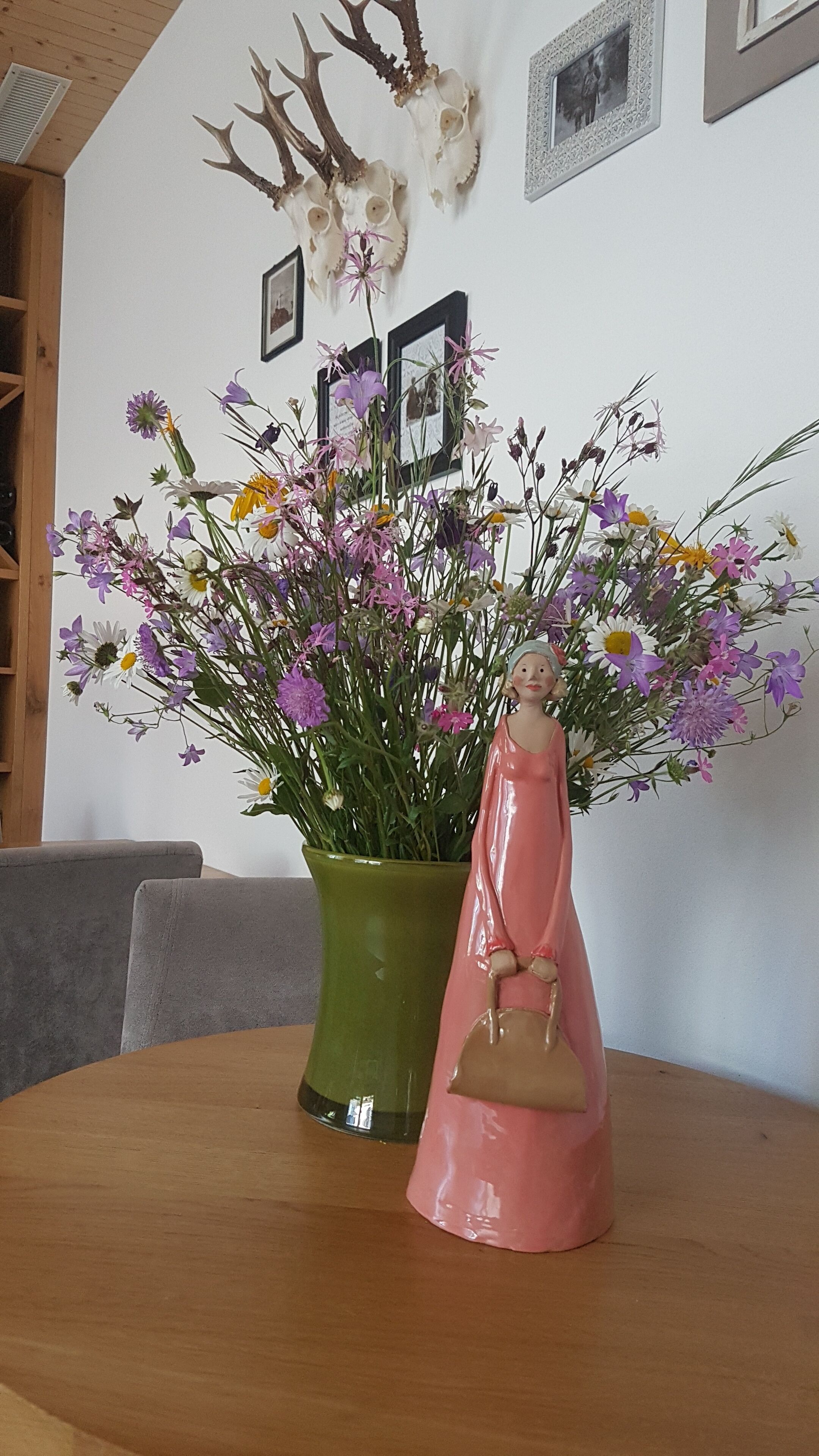 Una mesa con un florero verde de flores y una figurita rosa.