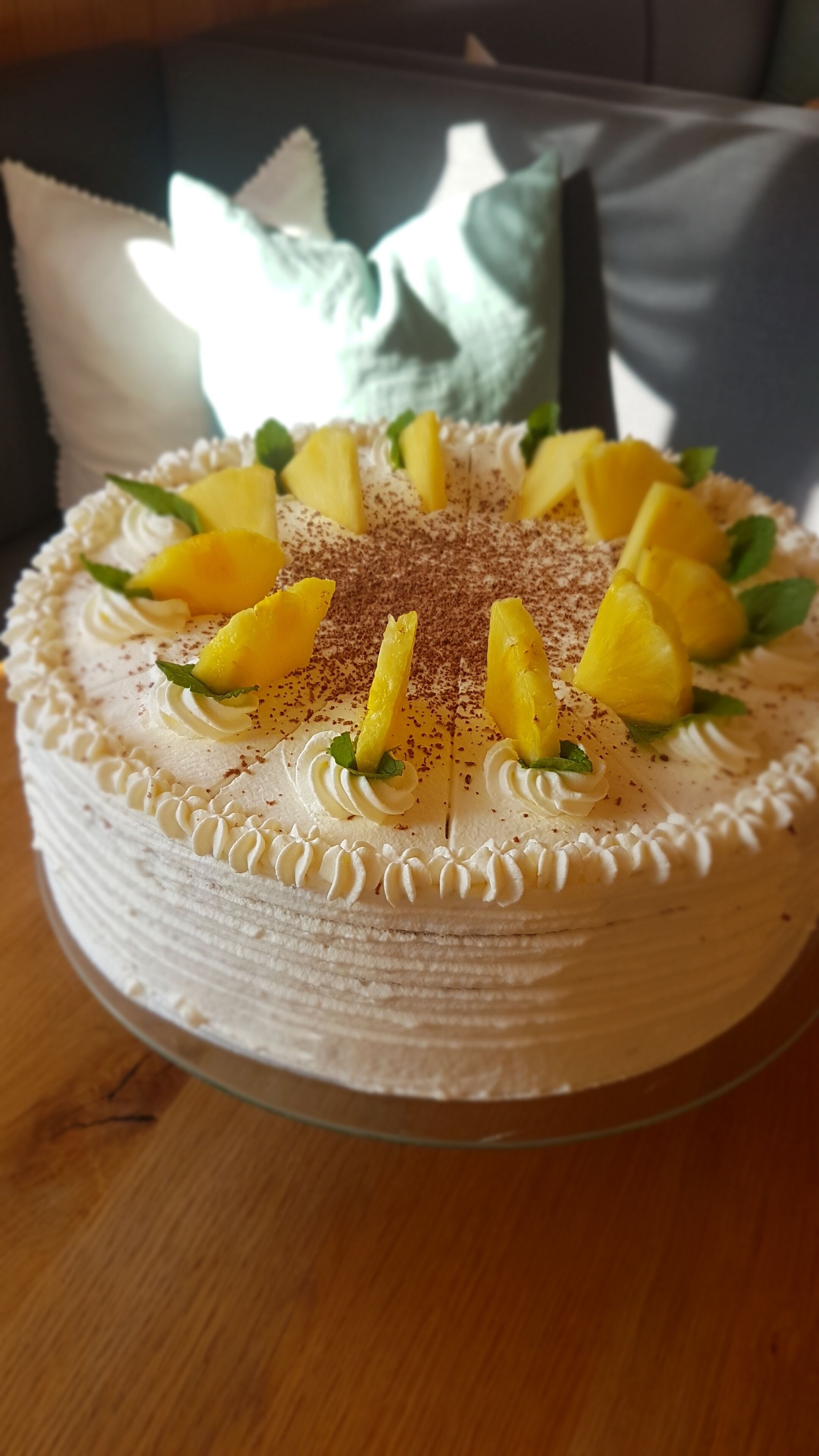 Un pastel redondo con cobertura blanca y rodajas de piña sobre un soporte de vidrio.