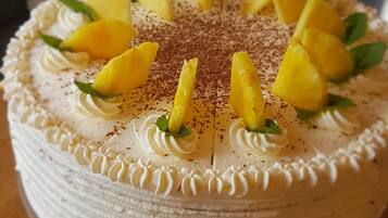 Un pastel redondo con cobertura blanca y rodajas de piña sobre un soporte de vidrio.