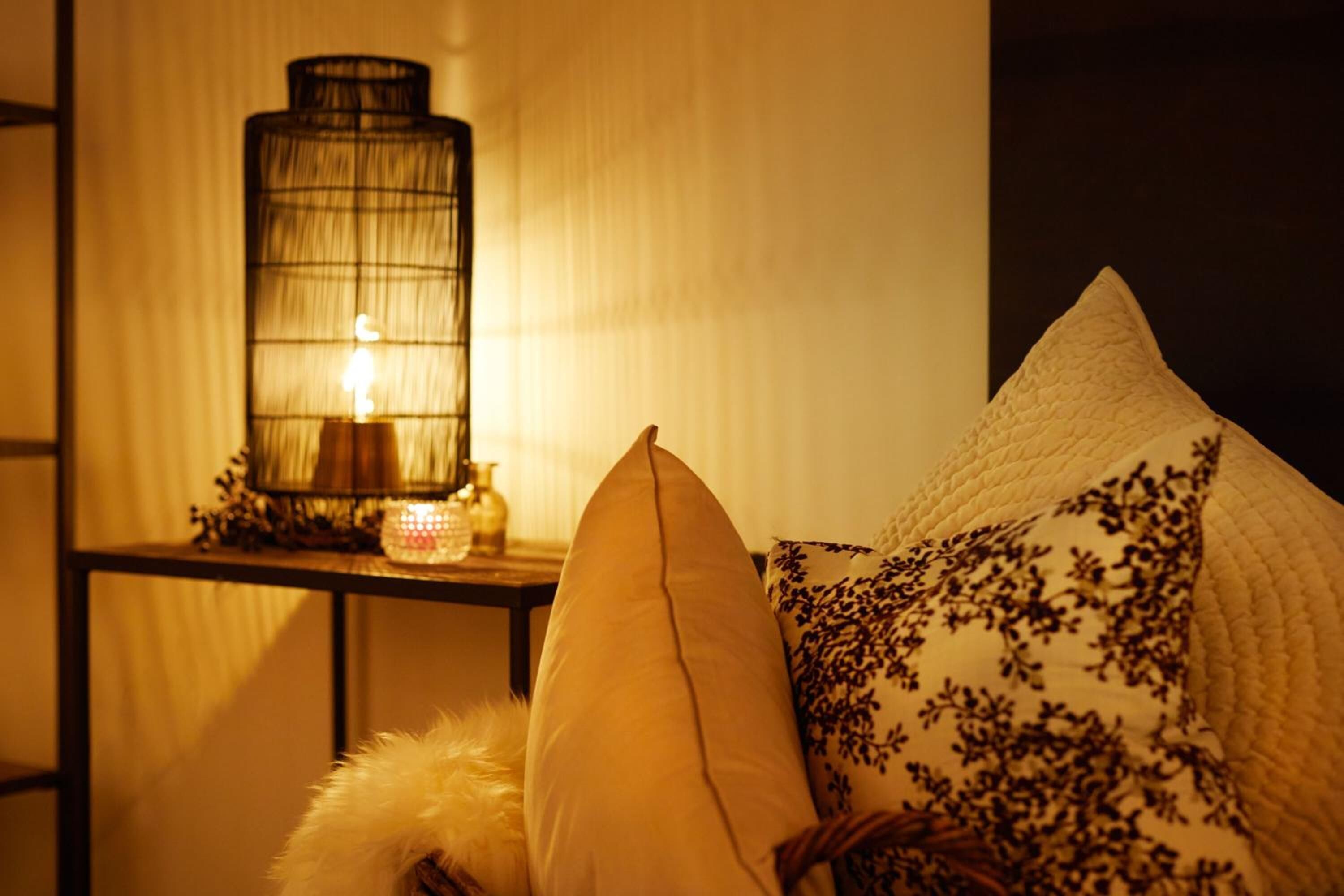 A cozy room with a lamp, a cushioned chair, and a decorative pillow.