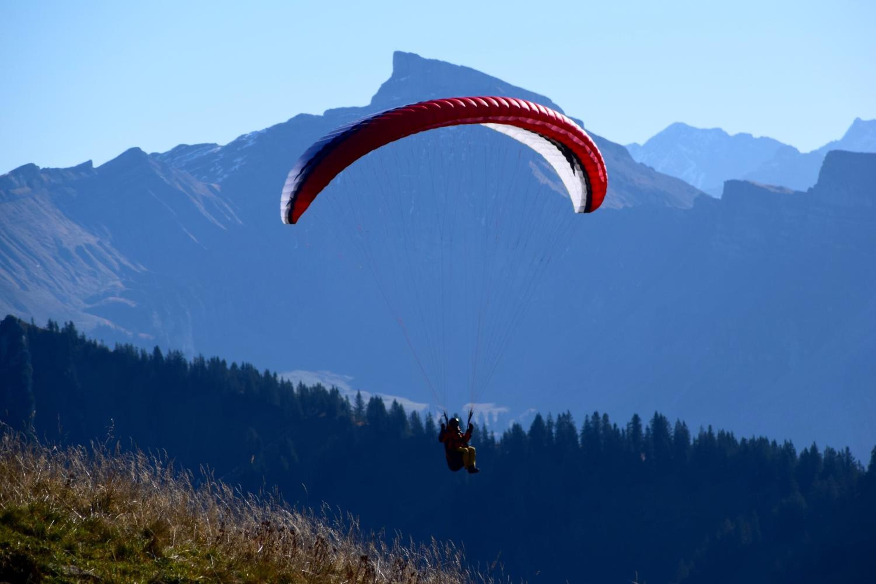 Un parapentista con un paracaídas rojo y blanco vuela sobre un paisaje montañoso.