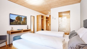 A modern bedroom with a wooden ceiling, a large bed with white linens, a desk with a computer, and a wall-mounted TV.