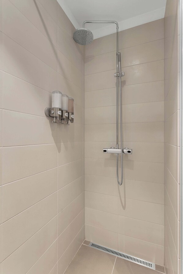 A shower with a handheld showerhead, a wall-mounted faucet, and a handheld soap dispenser. - SIF Apartments Central Reykjavik - 1 Bedroom (Reykjavík)