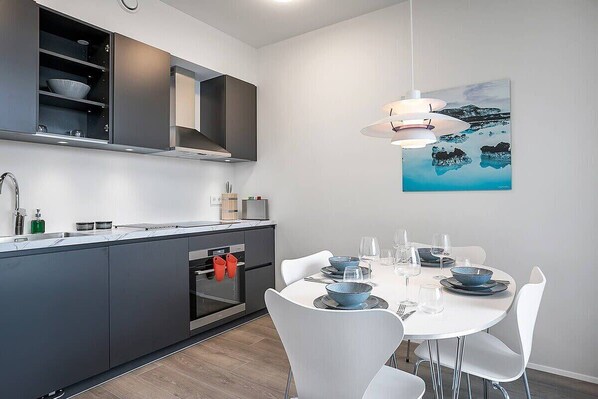 A modern kitchen with grey cabinets, a built-in oven, and a dining area with white chairs and a table set for four.