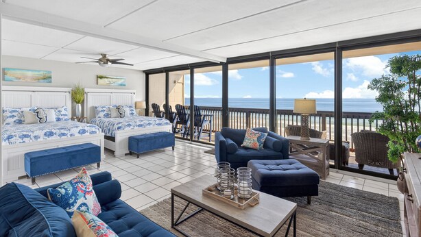 A spacious balcony with a view of the ocean, furnished with blue sofas, a coffee table, and a dining area. - Gulf Shores 506 Fifth Floor Beachfront View 2 Bedroom 2 Bathroom Condo (Port Aransas)