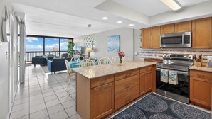 A modern kitchen with a large island, stainless steel appliances, wooden cabinets, and a view to the outside. - Gulf Shores 506 Fifth Floor Beachfront View 2 Bedroom 2 Bathroom Condo (Port Aransas)