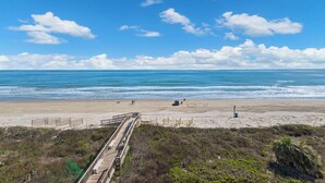 A beach with a wooden boardwalk leading to the shore, clear skies, and calm ocean waves. - Gulf Shores 506 Fifth Floor Beachfront View 2 Bedroom 2 Bathroom Condo (Port Aransas)