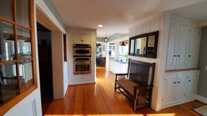 A kitchen with built-in ovens, a dining area with a bench, and a mirrored cabinet wall. - 1818 Modern Farm House with Pool, Hot Tub and a large permanent dock on the lake (Canandaigua)