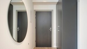 Een gang met een donker houten deur, een ronde spiegel links en een grijze garderobe rechts.