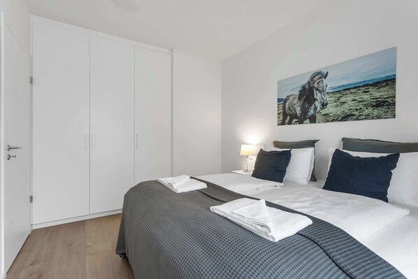 A hotel room with a bed, a painting of a horse, and a door.