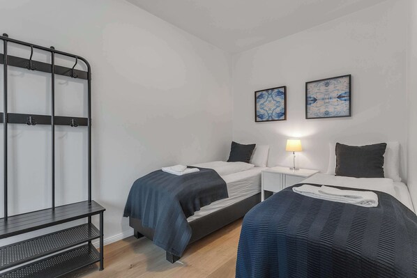 Hotellihuone, jossa on kaksi sänkyä, pieni pöytä, penkki ja kaksi seinälle ripustettua taideteosta.