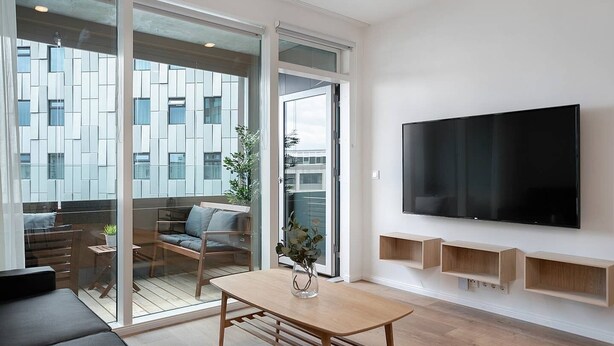 Una sala de estar moderna con un televisor grande, muebles de madera y un ventanal que da a un espacio al aire libre.