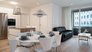 A modern kitchen with a built-in oven, a dining area with a round table and white chairs, and a black leather sofa.