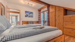 A bedroom with a large bed, wooden wardrobe, and a view of the mountains through the window.