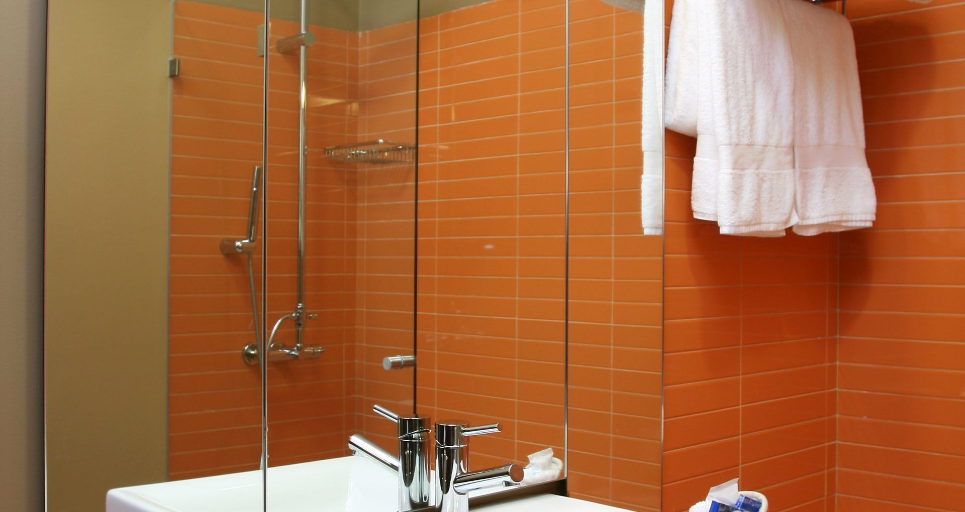 A bathroom with orange tiled walls, a white sink, and a glass shower enclosure.