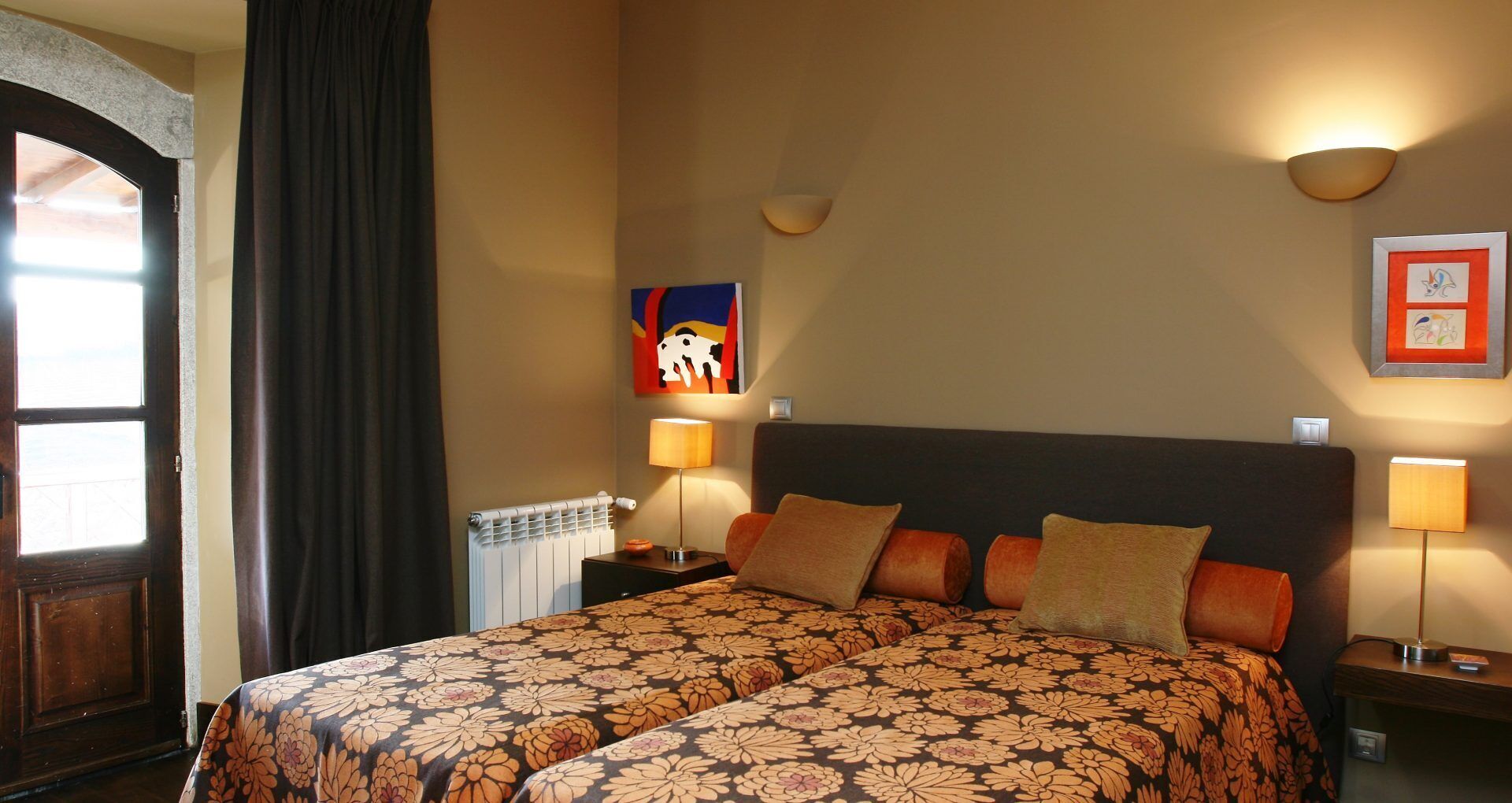 Une chambre d’hôtel avec un grand lit, deux lampes de chevet, un radiateur et une porte avec un rideau.