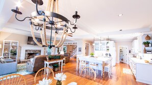 A spacious living room with a fireplace, a chandelier, and a dining area with white furniture. - Lovely Lake Escape on Lake Oconee with game room, hot tub and fire pit (Eatonton)