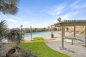 Relax by the pool surrounded by lush greenery and a wooden pergola.