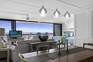 Enjoy ocean views from the large window in this stylish room, featuring a dining area with a table and chairs, a comfortable sofa, and a mounted TV.