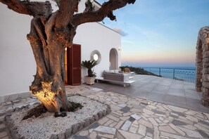 Ein moderner Außenbereich mit Steinfassade, einem Baum und Blick aufs Meer.