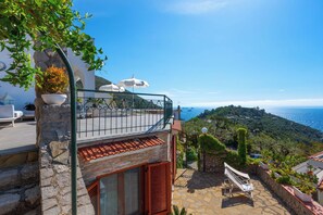 Un balcon avec un mur en pierre, une chaise blanche et une vue sur la mer.