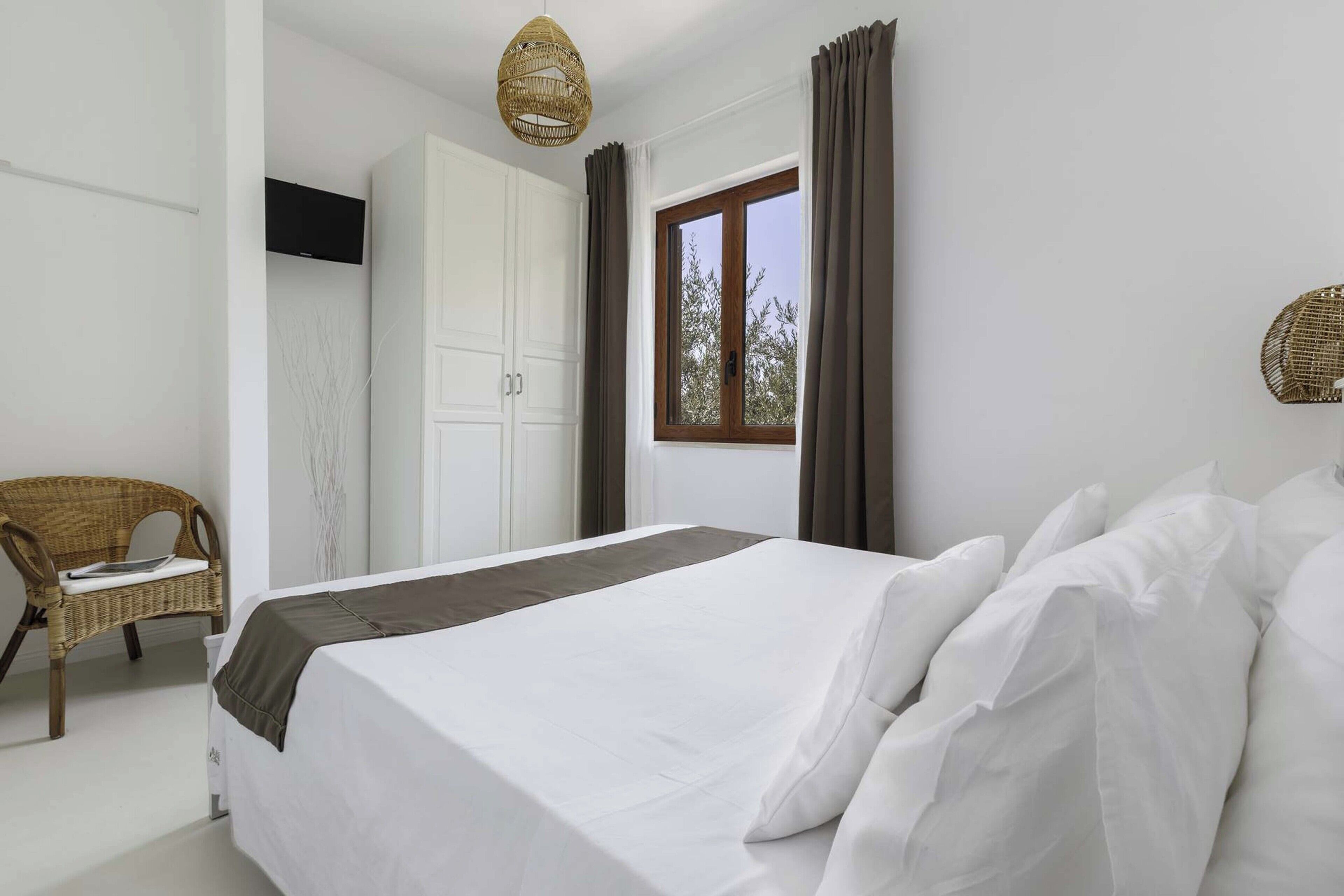 A bedroom with a bed, a chair, a wardrobe, and a window.