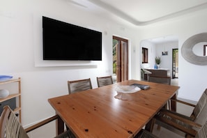 Ein Essbereich mit Holztisch, Stühlen, einem an der Wand befestigten Fernseher und Blick ins Freie.