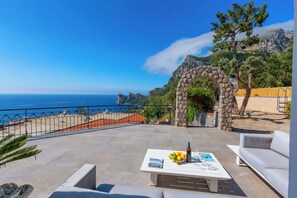 A terrace with a stone archway, outdoor seating, a table with a bottle and glasses, and a view of the sea. - Villa Marina with Private Pool, Sea View, Terraces and Parking (Nerano)