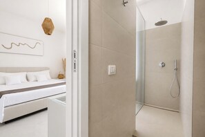 Ein modernes Badezimmer mit Duschkabine aus Glas, einem Bett mit weißer Bettwäsche und einer wandmontierten Leuchte.