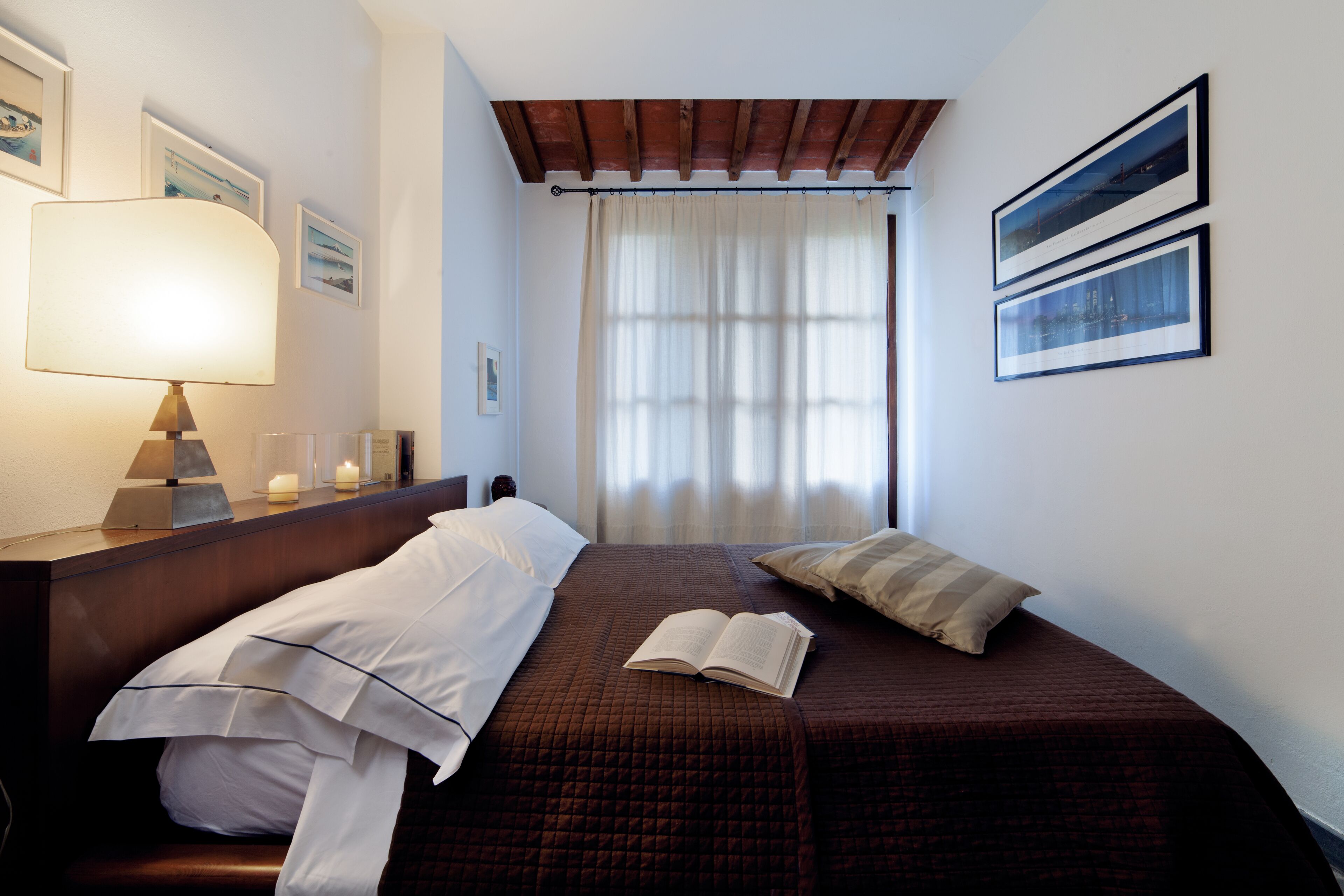 A neatly made bed with a brown bedspread and a white pillow, a bedside lamp, and a book on the bed.