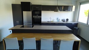 Een moderne keuken met een centraal eiland, vier witte stoelen en een raam dat natuurlijk licht binnenlaat.