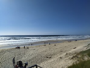 A beach with people walking and playing, a sandy shore, and waves crashing onto the beach.