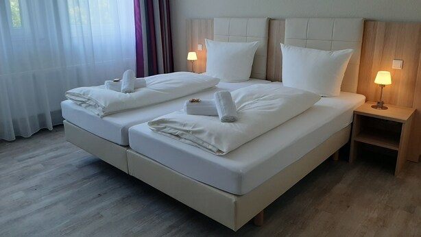 Una cama doble con sábanas y toallas blancas, dos lámparas de noche y un cabecero de madera.