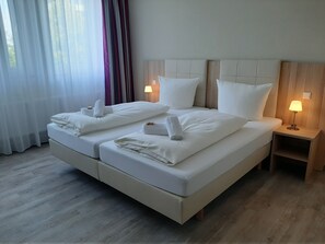 A double bed with white linens and towels, two bedside lamps, and a wooden headboard.