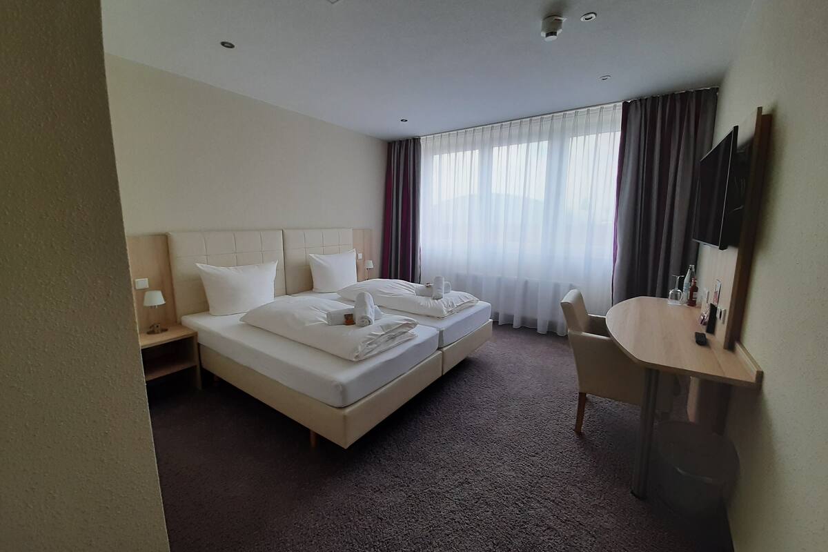 A hotel room with a large bed, a desk, and a chair.