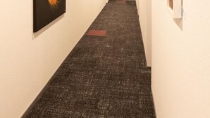 Un pasillo con obras de arte en las paredes, suelo alfombrado e iluminación empotrada en el techo.