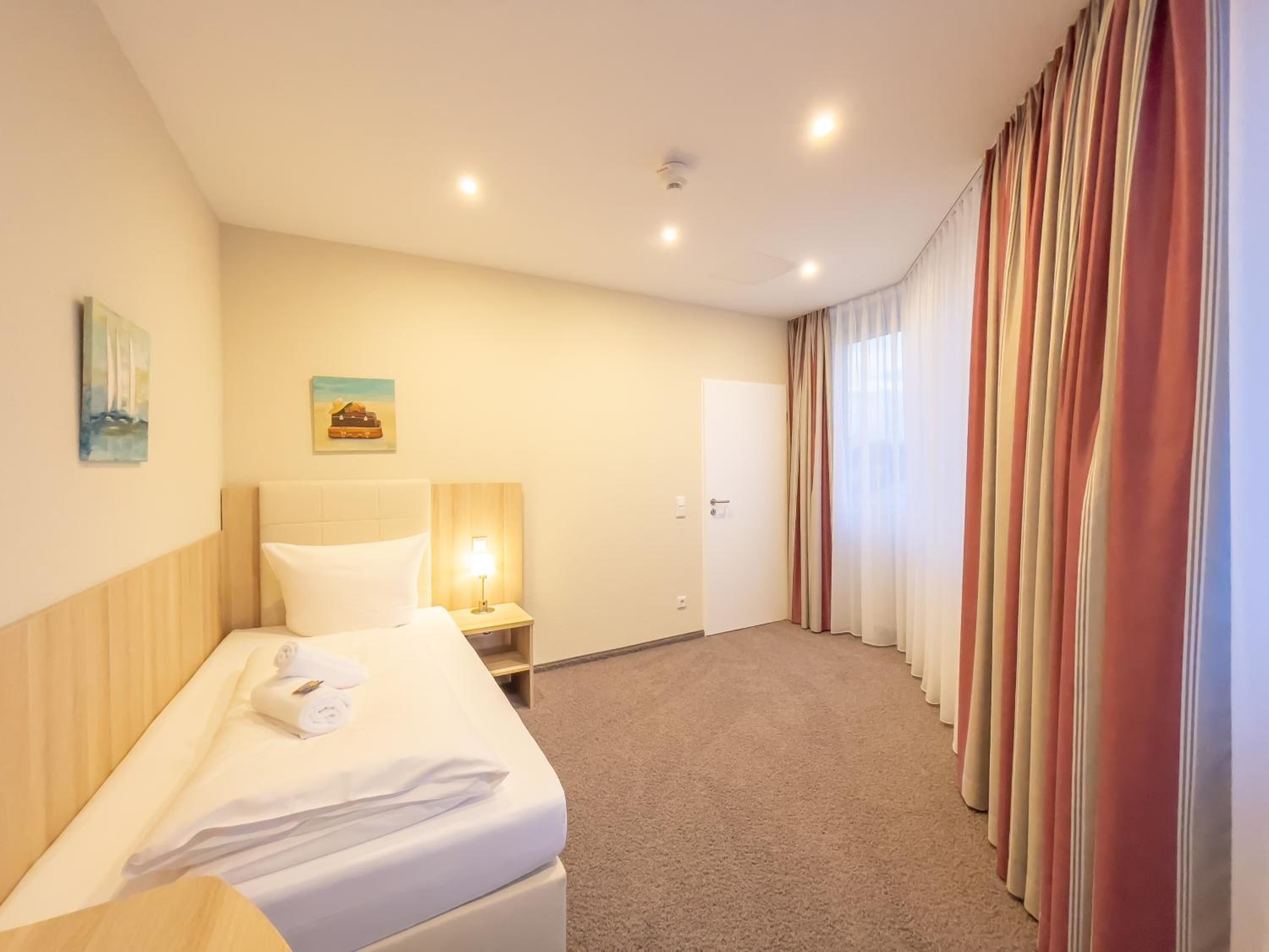 A hotel room with a bed, a nightstand with a lamp, a door, and a curtain.