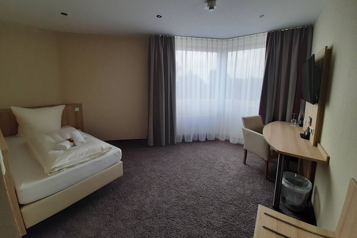 A hotel room with a bed, a desk, a chair, a TV, and a window with curtains.