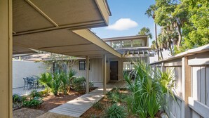Un área de patio techada con piso de madera, mobiliario exterior y diversas plantas.